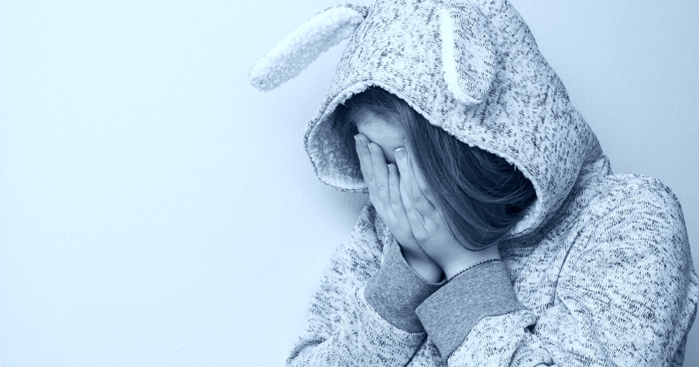 Pictured: a girl wearing a hoodie with bunny ears with her face in her hands