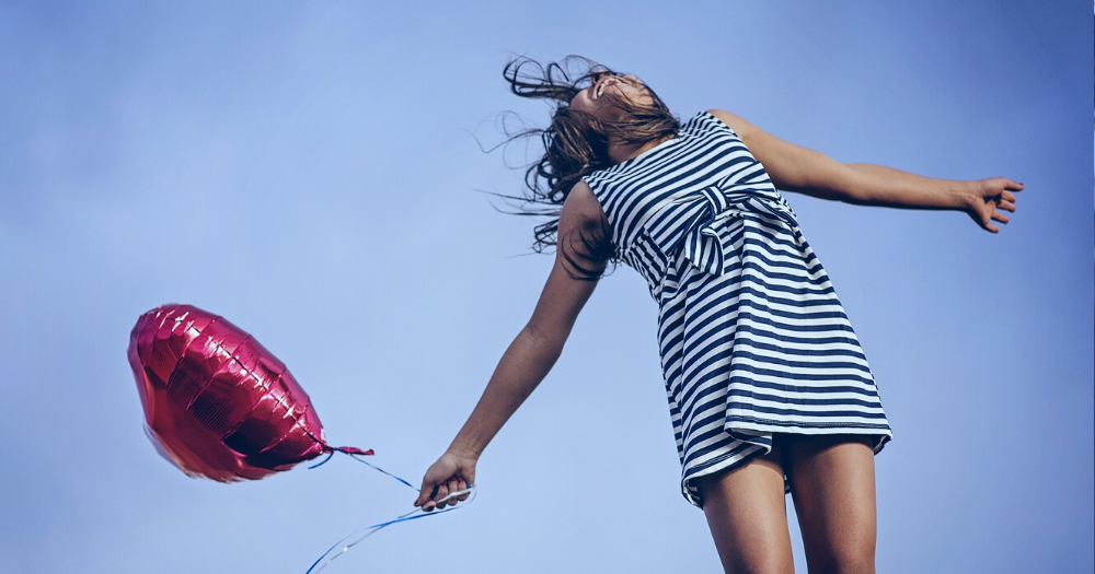 Breaking free of depression. Pictured: a happy girl holds a red balloon against a blue sky